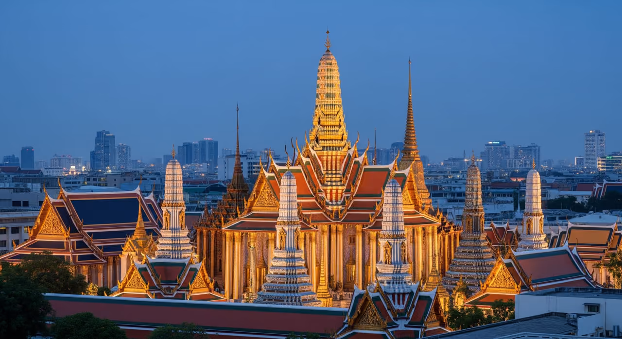 Osvětlené věže Grand Palace a Wat Phra Kaew zářící proti obloze Bangkokua za soumraku
